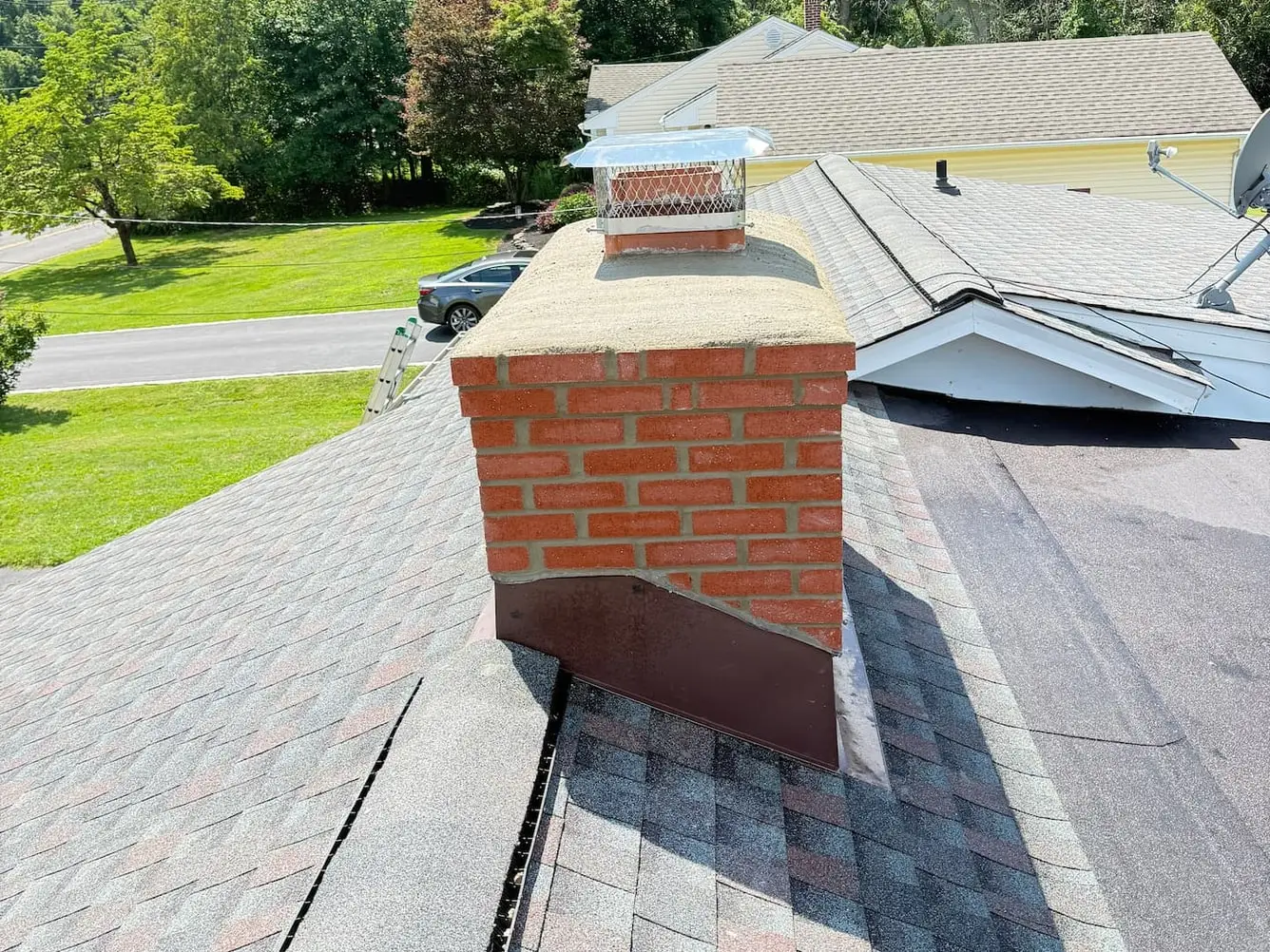 Brick chimney with new metal flashing around its base, a fresh crown and a metal cap, on a shingle roof