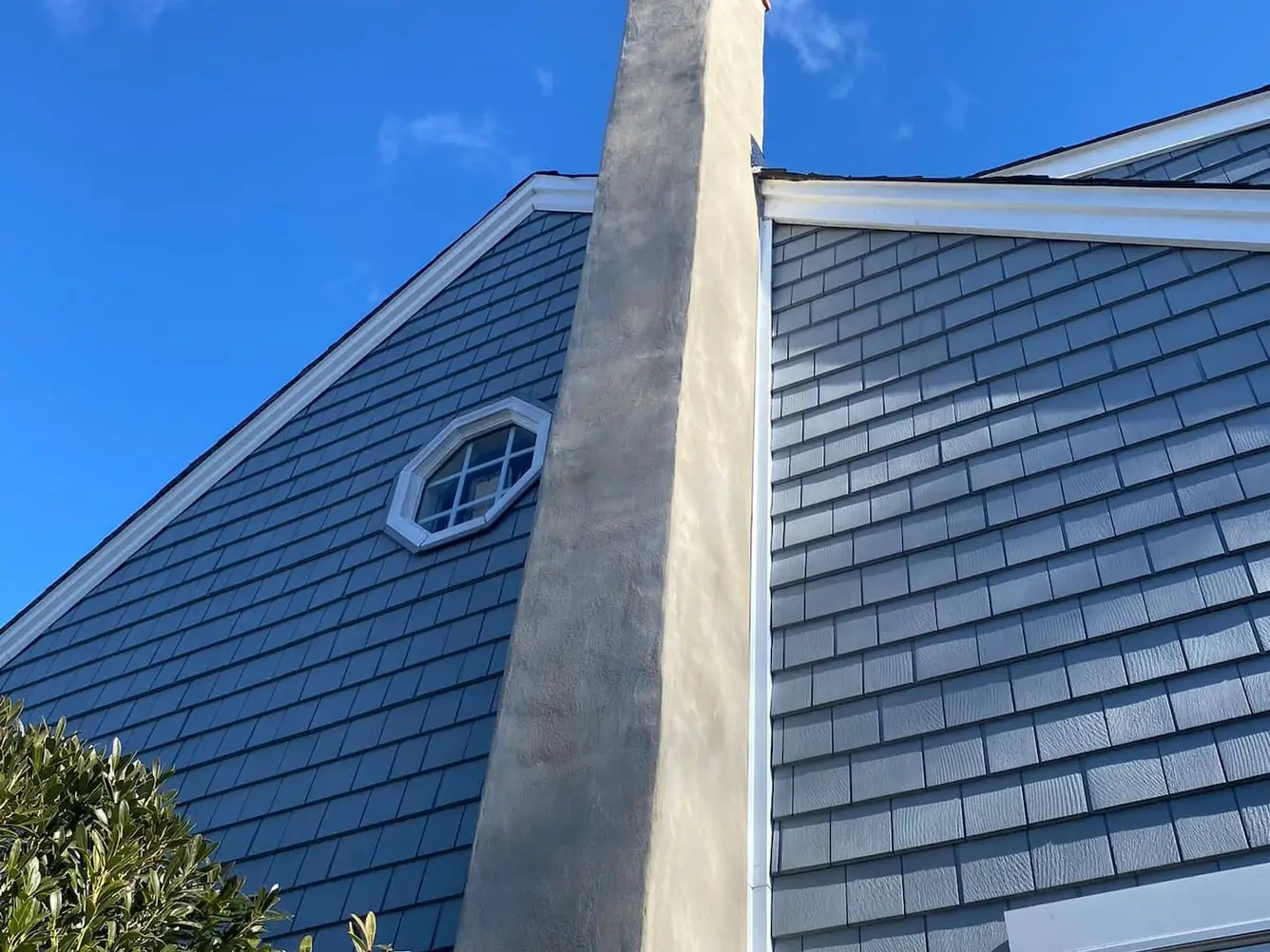 Rebuilt and parged chimney stack with a new metal crown, rising past shake siding