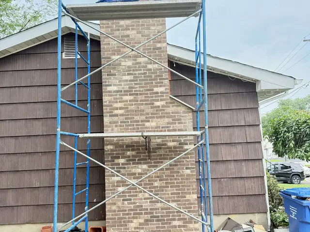 Scaffolding set up against a tall brick chimney on the side of a house with dark shake siding