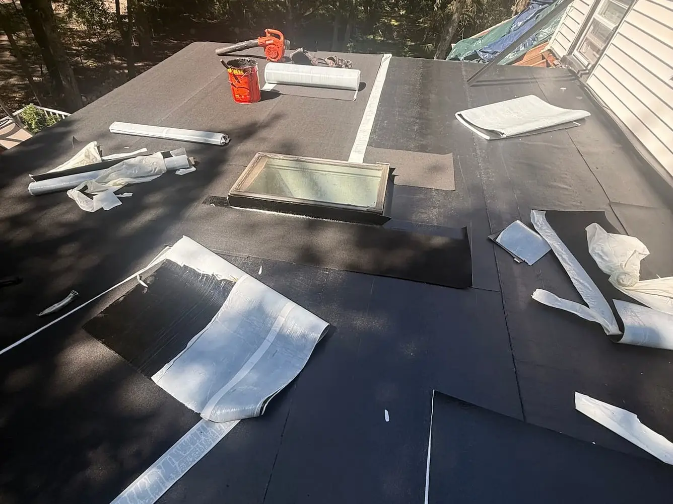 Low slope roof covered in black membrane, with a skylight set into it and rolls of membrane laid out