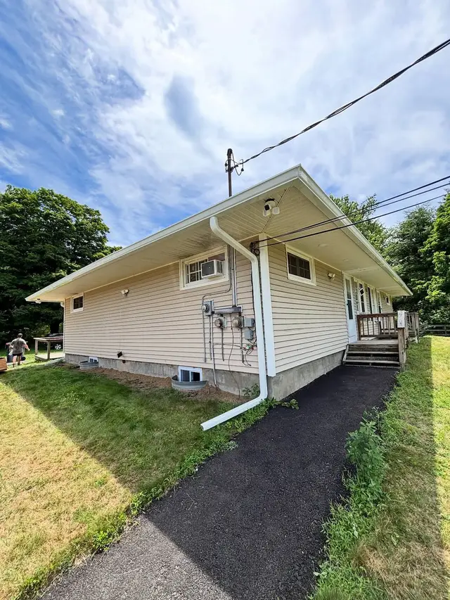 Single story house with tan vinyl siding, a white gutter along the eave and a downspout with an extension carrying water out onto the lawn