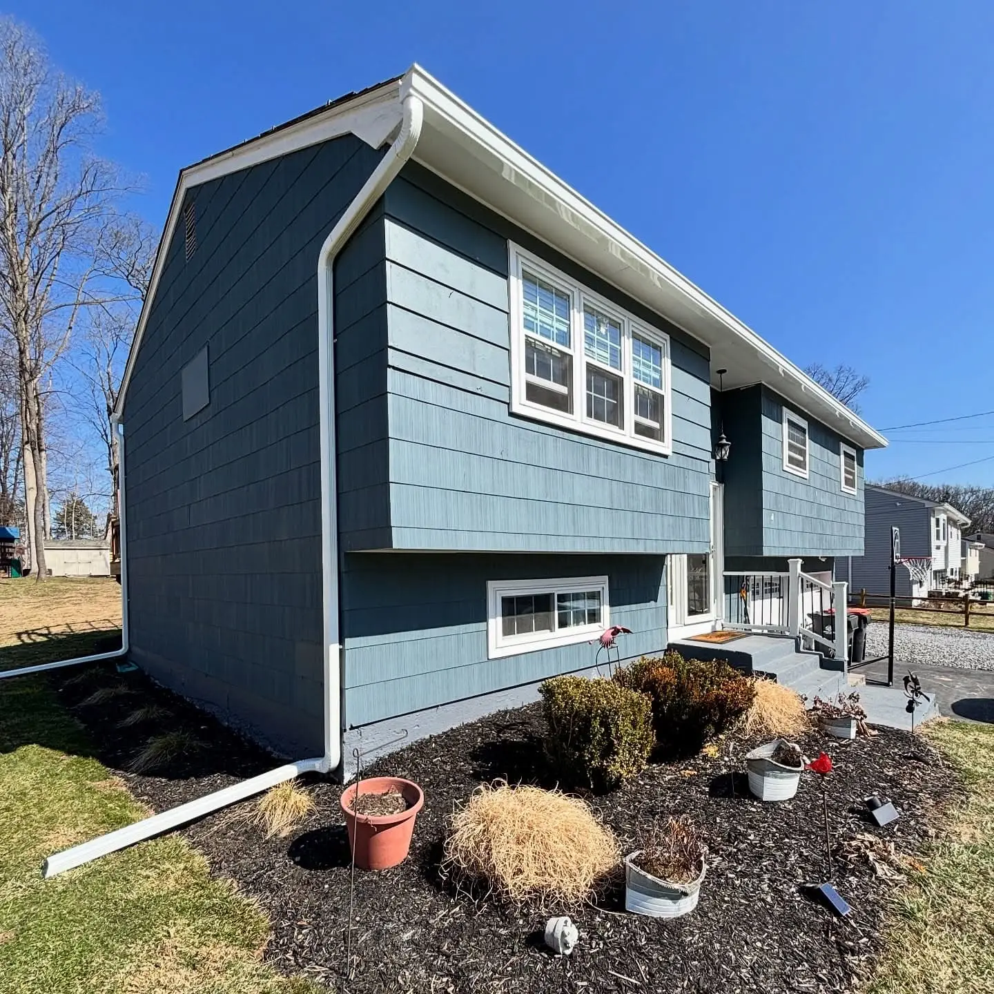 Split level house with blue shingle siding, white gutters along the eaves and downspouts with extensions running out across the garden bed