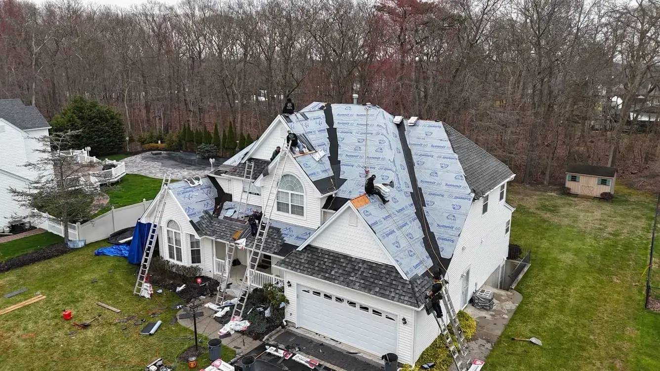 Aerial view of a two storey house mid tear off, with synthetic underlayment across several roof planes and a crew working on ladders
