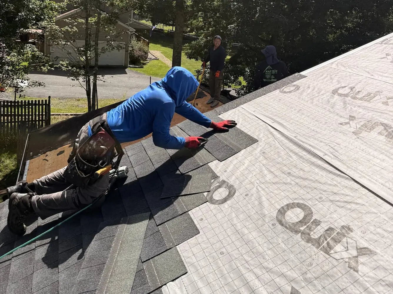 Roofer laying the first courses of new shingles over synthetic underlayment while two crew members work further along the roof