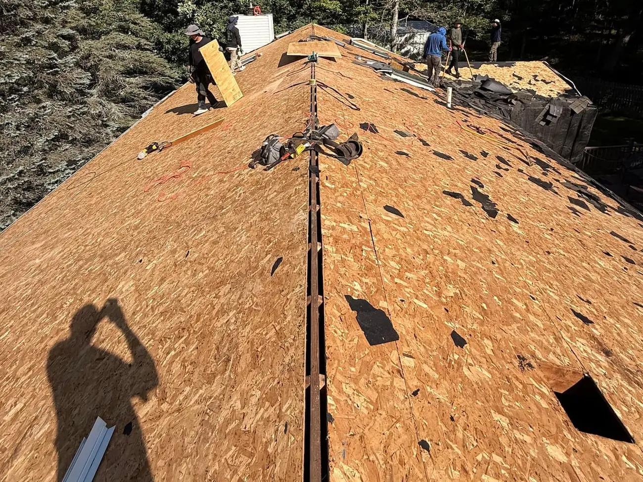 Roof stripped to new plywood decking with a continuous slot cut along the ridge and crew members working near the peak