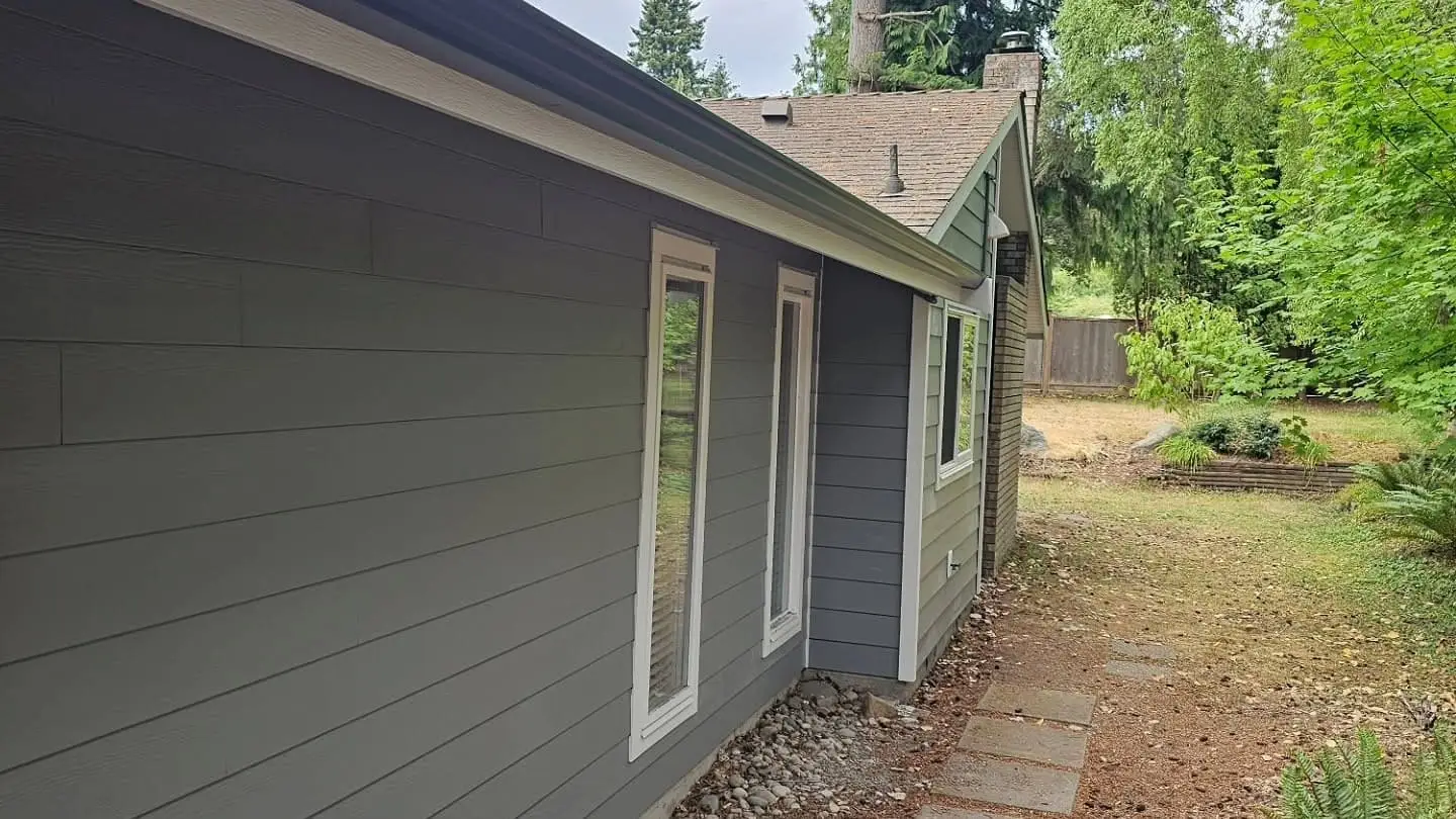 Gray lap siding running the length of a single story house, with white trimmed windows and a stone path beside it